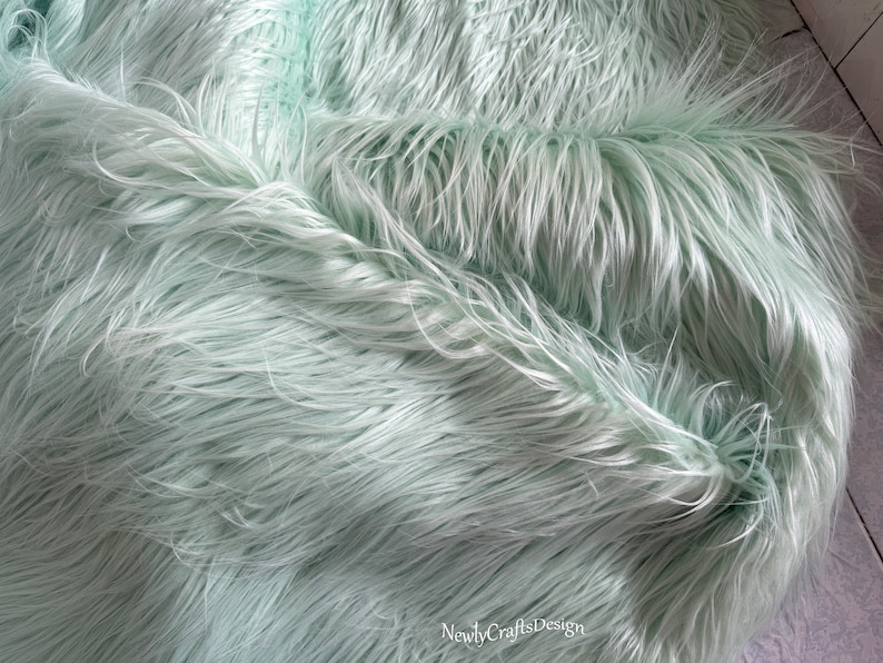 May include: A close-up of a light green faux fur fabric. The fabric is soft and fluffy, with a long pile.