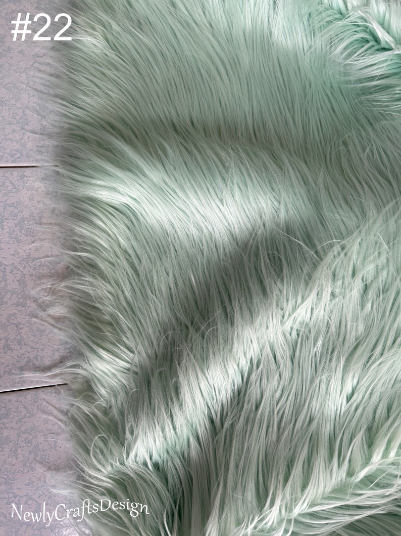May include: A close-up of a light green faux fur fabric. The fabric has a soft, fluffy texture and is perfect for crafting projects.