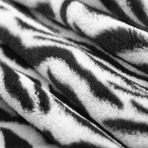 May include: Close-up of a soft, white and black patterned fabric with a fuzzy texture. The fabric has a zebra-like pattern.