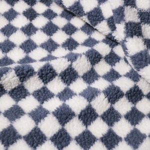 May include: A close-up of a soft, blue and white checkered fabric with a fuzzy texture. The fabric is made of a plush material and has a checkered pattern.