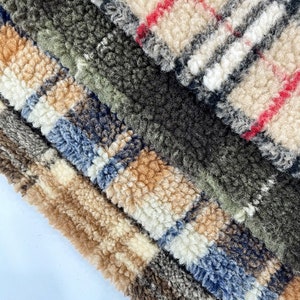 Puede incluir: Primer plano de una tela multicolor con textura peluda. La tela está hecha de diferentes tonos de marrón, beige, negro, blanco y rojo. La tela tiene un patrón de cuadros.