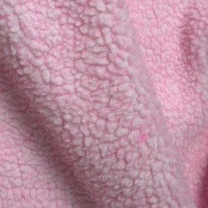 May include: Close-up of a soft, pink, fuzzy fabric with a textured surface. The fabric is a type of fleece.