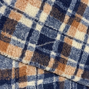 Könnte beinhalten: Nahaufnahme eines blauen, braunen und weißen karierten Stoffes mit einer flauschigen Textur. Der Stoff ist weich, plüschig und perfekt für Bastelprojekte.