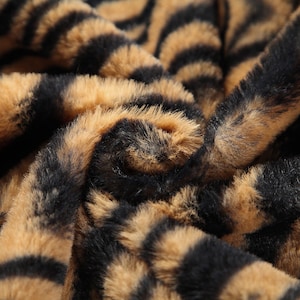 May include: Close-up of a brown and black faux fur fabric with a tiger stripe pattern.