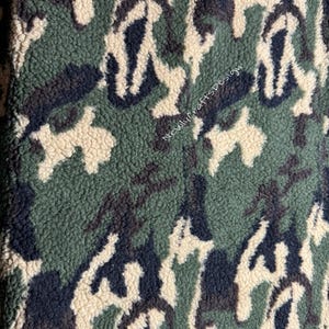May include: Close-up of a camouflage pattern fabric in shades of green, navy, and beige. The fabric has a textured, fuzzy surface. The number "#4" is in the upper left corner, and "NewlyCraftsDesign" is written diagonally across the fabric.