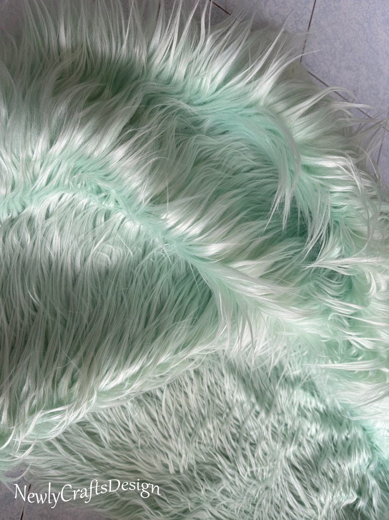 May include: A close-up of a light green faux fur fabric. The fur is soft and fluffy, with a subtle sheen.