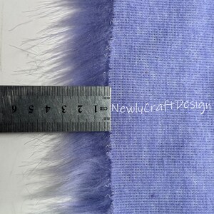 May include: A close-up of a purple faux fur fabric with a ruler measuring 9 inches. The fabric has a soft, fuzzy texture and is perfect for crafting projects.