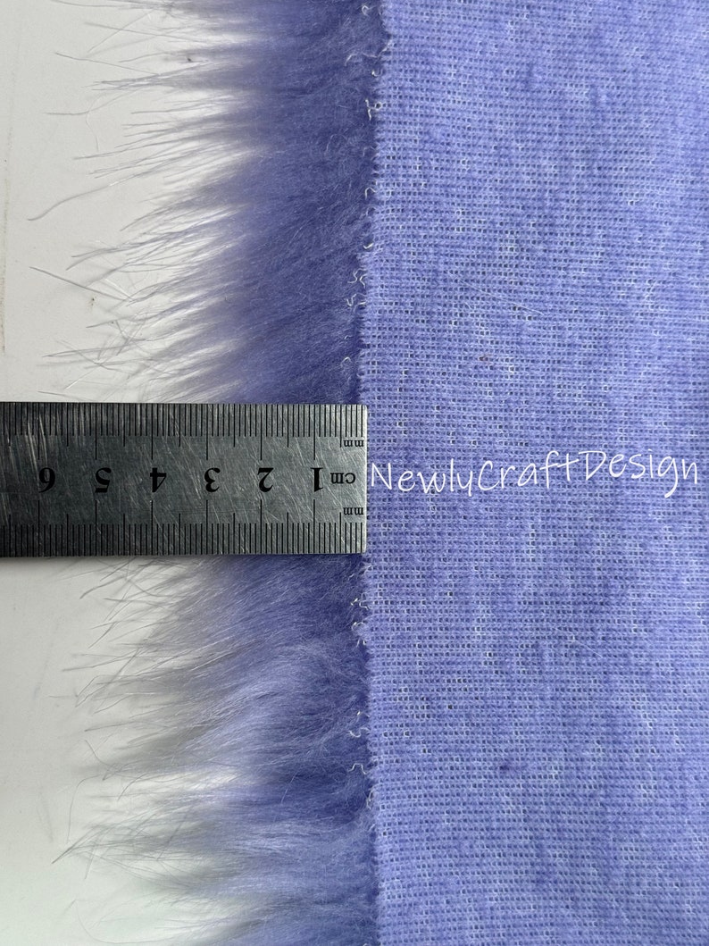 May include: A close-up of a purple faux fur fabric with a ruler measuring 9 inches. The fabric has a soft, fuzzy texture and is perfect for crafting projects.