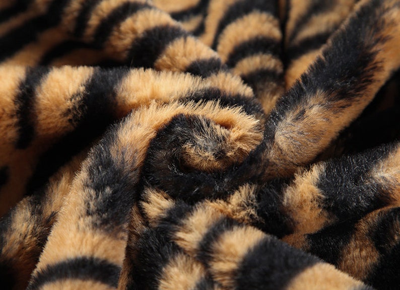 May include: Close-up of a brown and black faux fur fabric with a tiger stripe pattern.