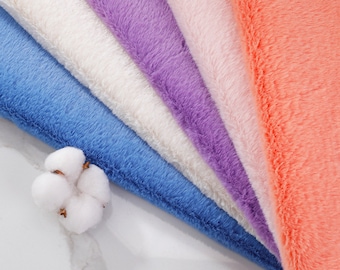 Peut inclure: Gros plan sur des échantillons de tissu doux et duveteux dans des tons pastel : bleu, blanc, lilas, rose et corail. Une fleur de coton est placée en bas à gauche, ajoutant une touche naturelle à l'ensemble.