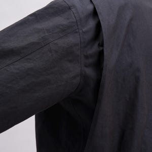 May include: Close-up of a black long-sleeved shirt. The image highlights the shoulder and sleeve details, showcasing the fabric's texture and stitching. The shirt appears to be made of a lightweight material.