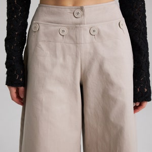 May include: Beige wide-leg cropped pants with a high waist and multiple button details.