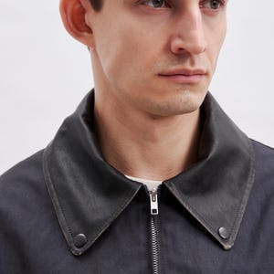 May include: A dark navy jacket with a black leather collar. The jacket has a silver zipper and a small pocket on the lower right side. The collar is buttoned on both sides.