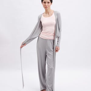 May include: A light gray open-front cardigan with long sleeves, a light pink scoop-neck tank top, and matching light gray wide-leg trousers. The outfit is paired with light pink ballet flats, creating a coordinated set of lounge clothing.