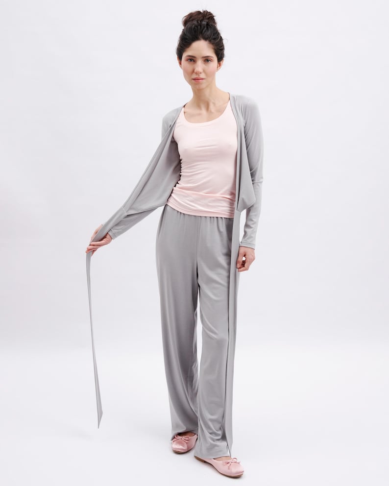 May include: A light gray open-front cardigan with long sleeves, a light pink scoop-neck tank top, and matching light gray wide-leg trousers. The outfit is paired with light pink ballet flats, creating a coordinated set of lounge clothing.