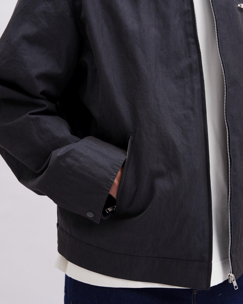 May include: A black jacket with a zipper closure and a pocket on the front. The jacket has a button closure on the pocket and a silver zipper. The jacket is made of a lightweight material.