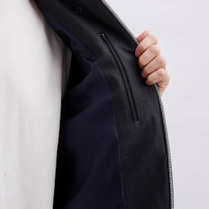 K&ouml;nnte beinhalten: Schwarze Jacke mit durchgehendem Rei&szlig;verschluss und marineblauem Innenfutter. Die Jacke hat eine Innentasche mit Rei&szlig;verschluss. Darunter wird ein wei&szlig;es T-Shirt getragen.