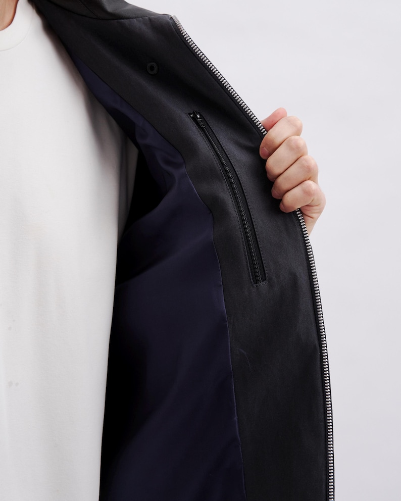 K&ouml;nnte beinhalten: Schwarze Jacke mit durchgehendem Rei&szlig;verschluss und marineblauem Innenfutter. Die Jacke hat eine Innentasche mit Rei&szlig;verschluss. Darunter wird ein wei&szlig;es T-Shirt getragen.