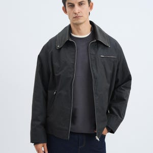 K&ouml;nnte beinhalten: Dunkelgraue Jacke mit Kragen und Rei&szlig;verschluss. Die Jacke wird &uuml;ber einem dunkelgrauen Sweatshirt getragen und mit dunkelblauen Jeans kombiniert. Das Model steht vor einem wei&szlig;en Hintergrund.
