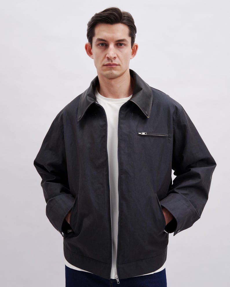 K&ouml;nnte beinhalten: Dunkelmarine Jacke mit schwarzem Lederkragen und silbernem Rei&szlig;verschluss. Die Jacke hat zwei Vordertaschen und ein wei&szlig;es T-Shirt darunter. Die Jacke ist ein l&auml;ssiger Stil.