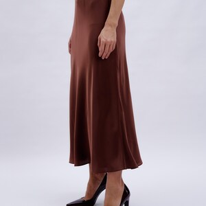 May include: A brown satin midi skirt with a slight A-line shape. The skirt is worn with a pair of dark burgundy heels.