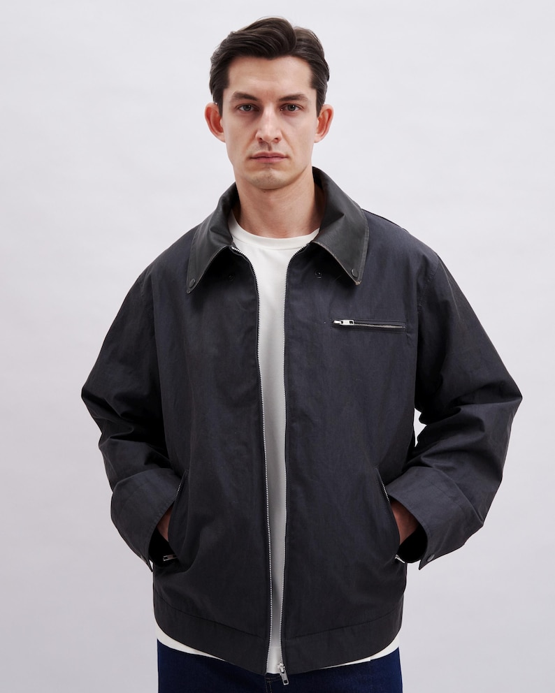 May include: Dark navy jacket with a black leather collar and a silver zipper. The jacket has two front pockets and a white t-shirt underneath. The jacket is a casual style.