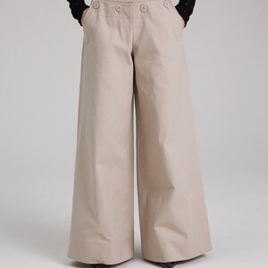 May include: Wide-leg, high-waisted pants in a light beige color with a button closure and flap pockets.