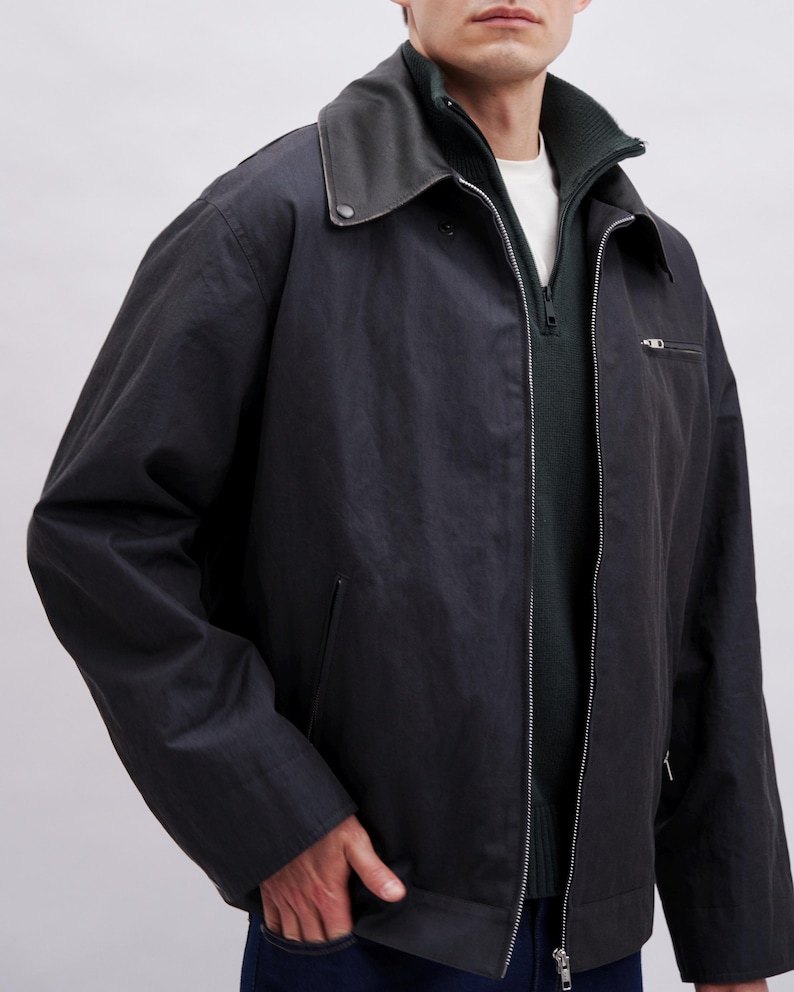 K&ouml;nnte beinhalten: Dunkelmarineblaue Jacke mit schwarzem Lederkragen und silbernem Rei&szlig;verschluss. Die Jacke hat einen Rei&szlig;verschluss vorne, eine kleine Brusttasche und zwei Seitentaschen. Das Model tr&auml;gt ein wei&szlig;es Hemd und einen gr&uuml;nen Pullover.