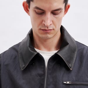 K&ouml;nnte beinhalten: Dunkelblaue Jacke mit schwarzem Lederkragen und silbernem Rei&szlig;verschluss. Die Jacke hat eine kleine Rei&szlig;verschlusstasche auf der Brust. Die Person im Bild tr&auml;gt ein wei&szlig;es T-Shirt darunter.