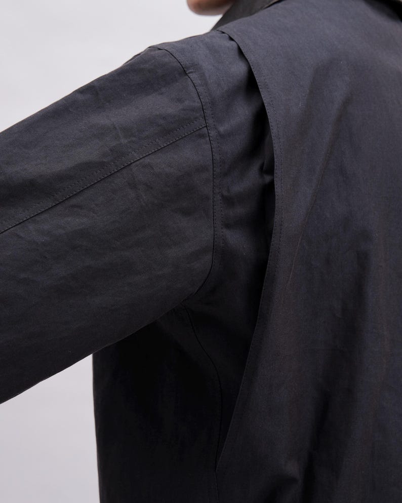 K&ouml;nnte beinhalten: Nahaufnahme eines schwarzen Langarmshirts. Das Bild zeigt die Schulter- und &Auml;rmeldetails und pr&auml;sentiert die Textur und die N&auml;hte des Stoffes. Das Shirt scheint aus einem leichten Material zu sein.