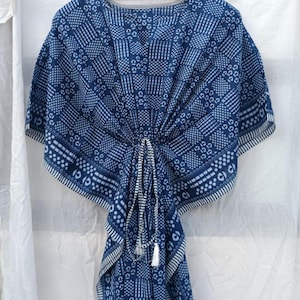 May include: A navy blue and white kaftan featuring a geometric block print pattern. The garment has short sleeves, a V-neckline, and a drawstring waist with white tassels that gathers the fabric at the center, creating a draped silhouette.
