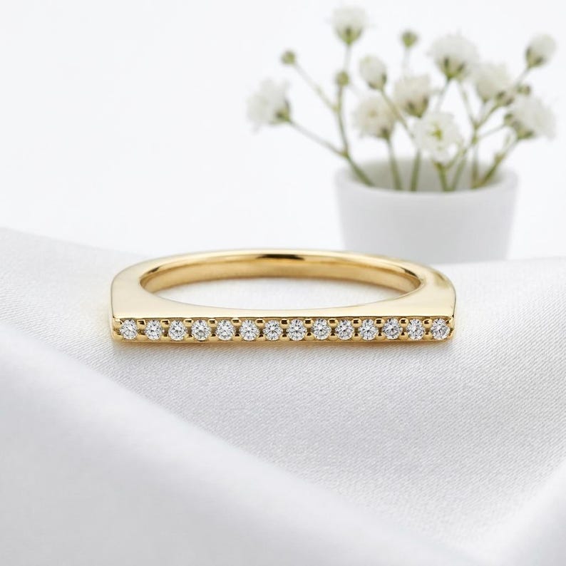 Puede incluir: Un anillo de oro con un dise&ntilde;o de barra horizontal plana engastado con una hilera de catorce piedras peque&ntilde;as, redondas, claras y brillantes. La banda es de oro amarillo pulido y las piedras est&aacute;n dispuestas en l&iacute;nea recta en la parte superior.
