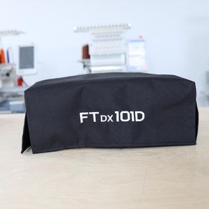Peut inclure: Housse en tissu noir avec broderie blanche indiquant "FT Dx 101D".
