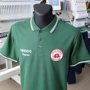 Könnte beinhalten: Ein grünes Poloshirt mit weißen Paspeln an Kragen und Ärmeln. Das Shirt hat ein weiß gesticktes Logo auf der linken Brust, das "Swiss DX Foundation" und "DXT - since 1998" lautet. Das Shirt hat auch ein weiß gesticktes Namensschild auf der linken Brust, das "HB9DDO Stephan" lautet.