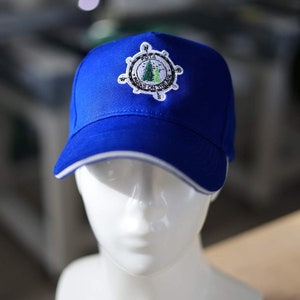 Könnte beinhalten: Eine blaue Baseballkappe mit weißem Schirm und einem weißen und grünen gestickten Logo mit der Aufschrift "POTA Parks on the Air" mit einem Kompassdesign.