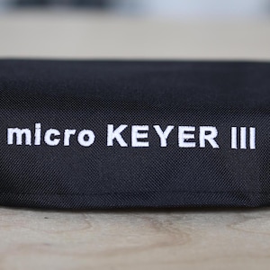 Peut inclure: Housse en tissu noir avec du texte blanc qui dit "micro KEYER III".