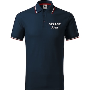 Peut inclure: Un polo bleu marine avec un col et des poignets rayés blanc et rouge. Le polo est orné d'un logo brodé blanc qui dit "3Z2ACE Alex".