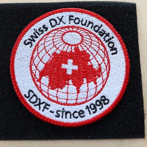 May include: A white embroidered patch with a red globe, a red Swiss cross, and the text "Swiss DX Foundation SDXF - since 1998".