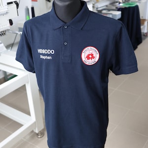 Könnte beinhalten: Ein marineblaues Poloshirt mit einem weißen gestickten Namensschild mit der Aufschrift "HB9DDO Stephan" und einem roten gestickten Logo mit der Aufschrift "Swiss Dr. Foundation SKKF - since 1998".