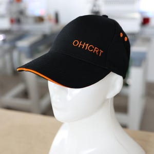May include: Black baseball cap with orange trim and embroidered text "OH1CRT". The cap has a curved peak and three orange dots on the side. The cap is displayed on a white mannequin head.
