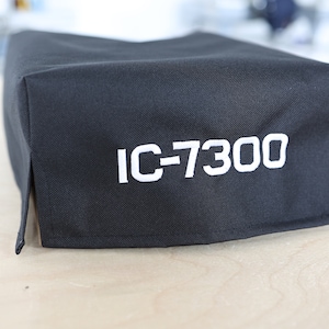 Pode incluir: Uma capa de tecido preto com o texto "IC-7300" bordado em branco.
