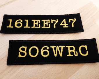 Könnte beinhalten: Zwei schwarze Stoffpatches mit goldfarbener Stickerei. Der obere Patch zeigt "161EE747" und der untere Patch zeigt "S06WRC".