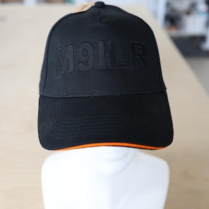 Op de afbeelding: Zwarte baseballcap met de in reliëf aangebrachte tekst "M91LR" op de voorkant. De cap heeft een oranje rand langs de rand en wordt getoond op een witte mannequinhoofd. De cap is gemaakt van een textuurstof.