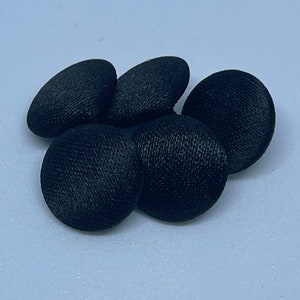 May include: Five black fabric covered buttons. The buttons are round and have a textured surface.