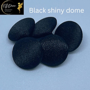 May include: A collection of five circular, black fabric-covered buttons with a shiny, domed surface. The buttons feature a smooth, satin-like texture and a rounded profile. The text "Elf Decor JOANNA ATTIA" and "Black shiny dome" is visible.