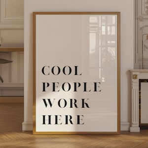 Może przedstawiać: Prostokątny wydruk ścienny w cienkiej złotej ramie z czarnym napisem COOL PEOPLE WORK HERE wyśrodkowanym na białym tle. Wydruk jest prezentowany w orientacji pionowej z wyraźnym, kontrastowym wzorem i pogrubioną typografią.