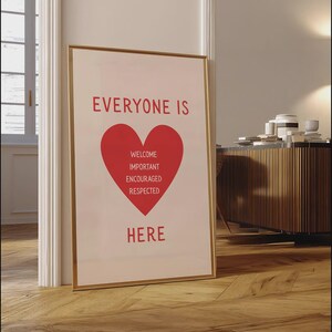 Może przedstawiać: Oprawiony plakat ze słowami "EVERYONE IS HERE" w kolorze czerwonym, z czerwonym sercem pośrodku. Wewnątrz serca znajdują się słowa "WELCOME, IMPORTANT, ENCOURAGED, RESPECTED". Rama jest złota.