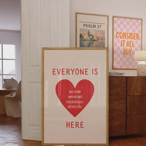 Może przedstawiać: Oprawiony plakat z czerwonymi słowami "EVERYONE IS HERE" i czerwonym sercem. Pod sercem znajdują się słowa "WELCOME, IMPORTANT, ENCOURAGED, RESPECTED." Widoczne są dwa inne oprawione dzieła sztuki.