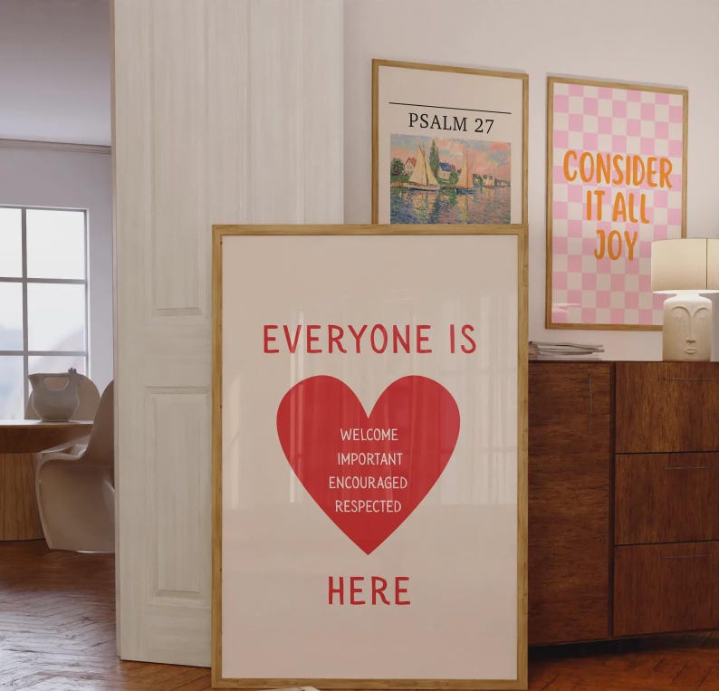 Może przedstawiać: Oprawiony plakat z czerwonymi słowami "EVERYONE IS HERE" i czerwonym sercem. Pod sercem znajdują się słowa "WELCOME, IMPORTANT, ENCOURAGED, RESPECTED." Widoczne są dwa inne oprawione dzieła sztuki.