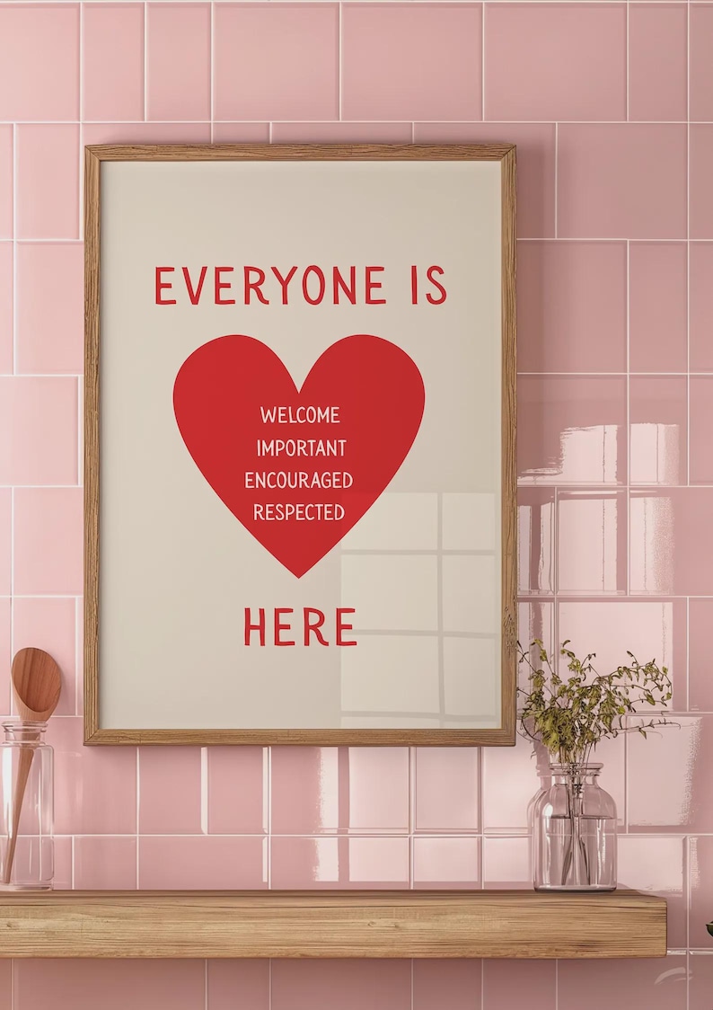 Może przedstawiać: Oprawiony wydruk z czerwonymi słowami "EVERYONE IS HERE", z czerwonym sercem pośrodku zawierającym słowa "WELCOME, IMPORTANT, ENCOURAGED, RESPECTED". Rama jest jasnobrązowa, na tle r&oacute;żowej kafelkowej ściany.